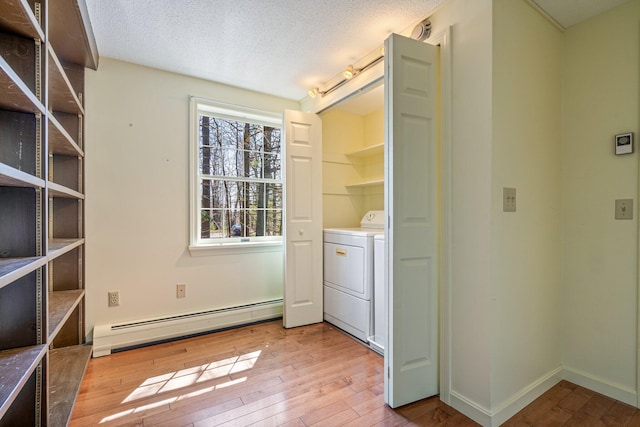 laundry area featuring laundry area, washer / dryer, baseboard heating, a textured ceiling, and light wood-style flooring