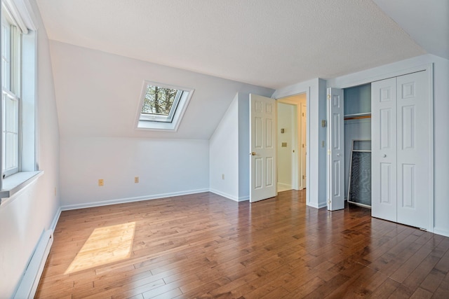 additional living space featuring a baseboard radiator, a textured ceiling, hardwood / wood-style floors, and a skylight