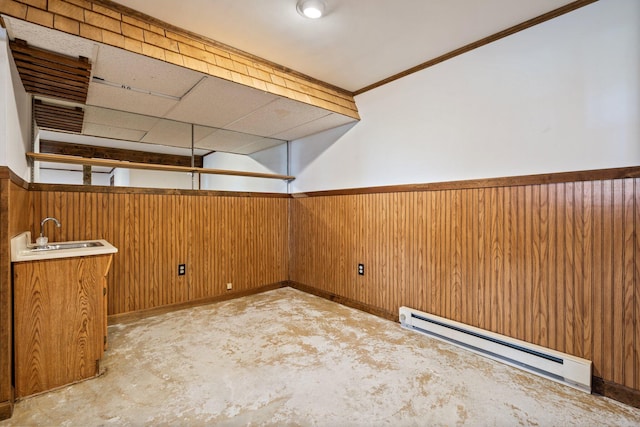 empty room featuring wooden walls, a sink, baseboard heating, a wainscoted wall, and wet bar
