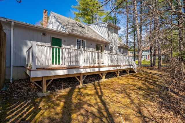 back of house featuring a deck, a chimney, and roof with shingles