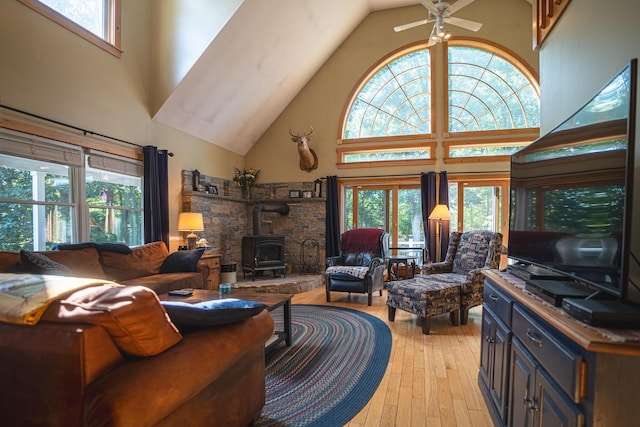 living area with a wood stove, light wood-style floors, a towering ceiling, and a healthy amount of sunlight