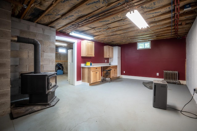 basement featuring a wood stove, radiator heating unit, baseboards, and concrete block wall