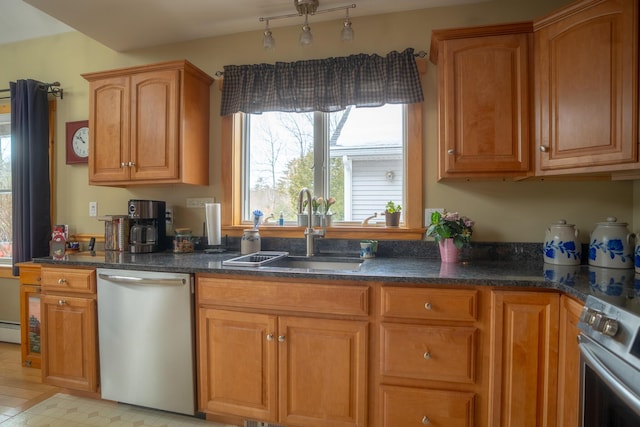 kitchen with baseboard heating, appliances with stainless steel finishes, brown cabinetry, a sink, and dark stone countertops