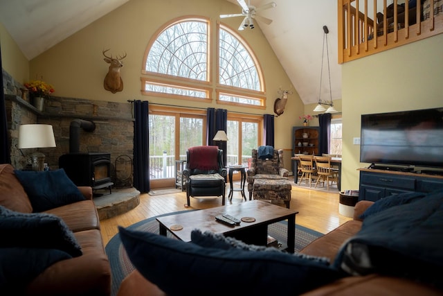 living area featuring ceiling fan, high vaulted ceiling, wood finished floors, and a wood stove