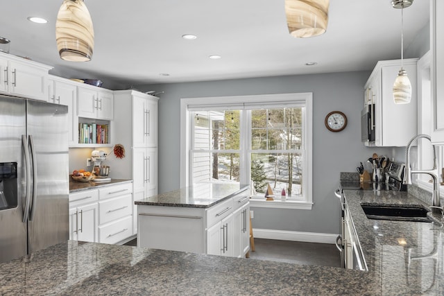 kitchen featuring appliances with stainless steel finishes, dark stone countertops, a sink, and white cabinets