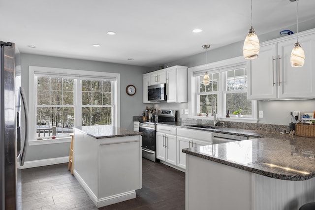 kitchen with a kitchen island, appliances with stainless steel finishes, dark stone countertops, white cabinetry, and a sink