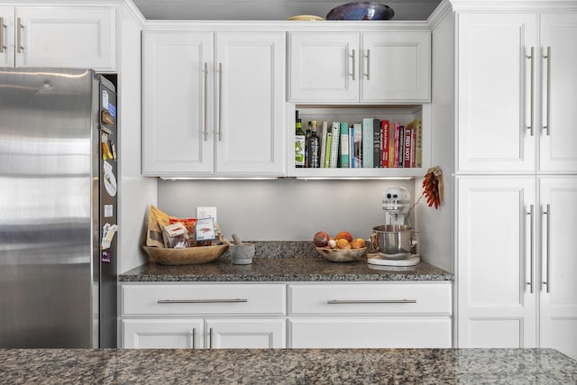 interior space featuring dark stone countertops, freestanding refrigerator, and white cabinetry