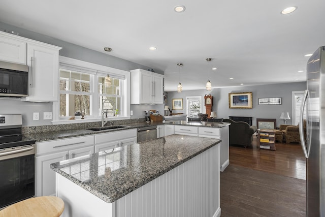 kitchen with dark wood finished floors, stainless steel appliances, open floor plan, a sink, and a peninsula