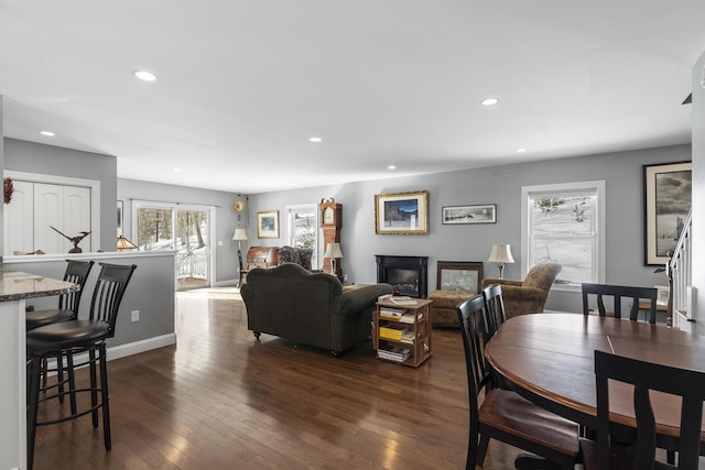 dining space with dark wood-type flooring, recessed lighting, a glass covered fireplace, and baseboards