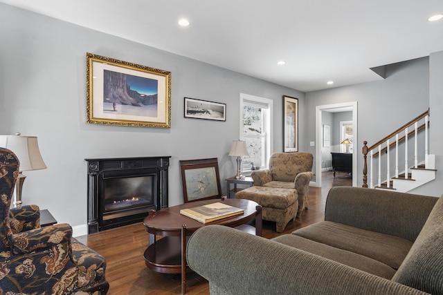 living area featuring baseboards, a glass covered fireplace, stairway, wood finished floors, and recessed lighting