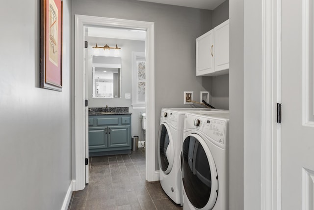 clothes washing area featuring cabinet space, washing machine and dryer, baseboards, and a sink