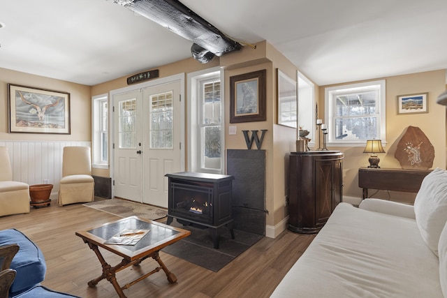 living room featuring french doors, a wainscoted wall, a wood stove, wood finished floors, and baseboards