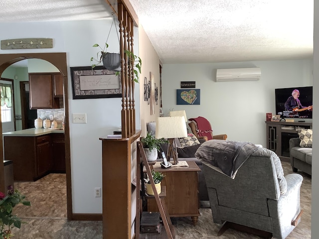 living area featuring a wall unit AC, baseboards, arched walkways, and a textured ceiling