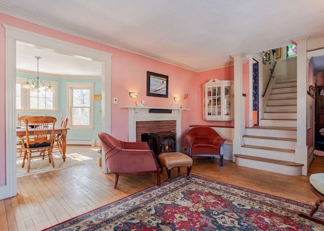 living area featuring a baseboard heating unit, stairs, a brick fireplace, wood-type flooring, and crown molding