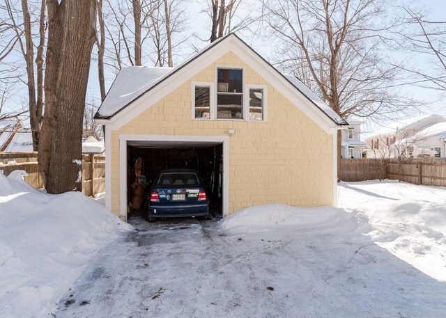 snow covered garage with a detached garage and fence