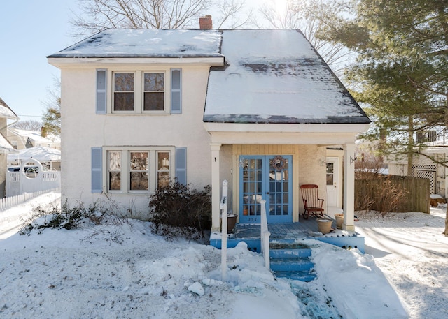 view of front of house featuring stucco siding, a chimney, fence, and french doors