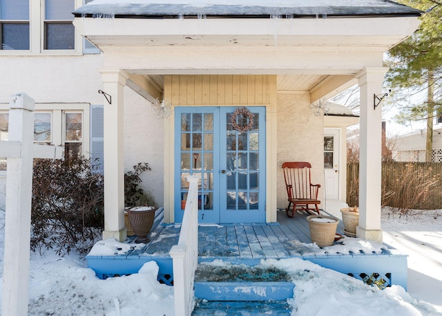 snow covered property entrance with stucco siding, fence, and french doors