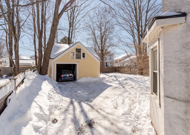 view of snowy exterior with a garage, fence, and an outdoor structure