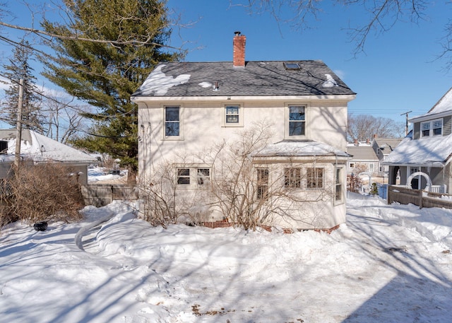 snow covered back of property featuring a chimney and stucco siding