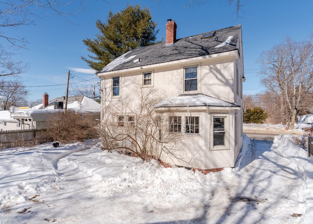 snow covered property with a chimney, fence, and stucco siding