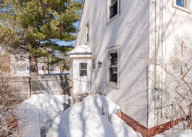 view of snow covered exterior with fence and stucco siding