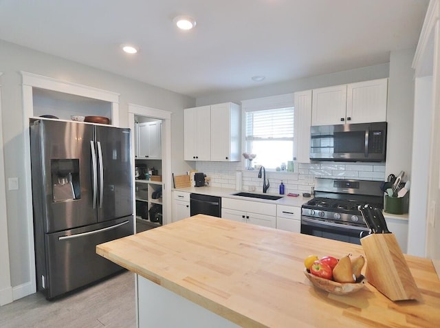 kitchen with tasteful backsplash, butcher block countertops, appliances with stainless steel finishes, white cabinetry, and a sink