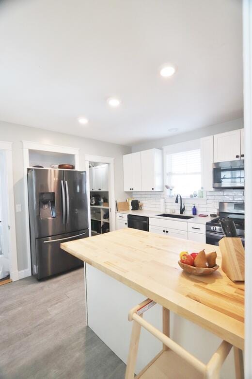 kitchen with appliances with stainless steel finishes, white cabinets, a sink, and decorative backsplash