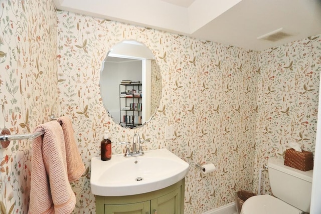 half bathroom featuring toilet, wallpapered walls, visible vents, and vanity