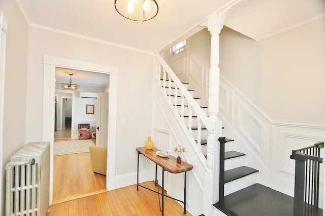 stairway featuring radiator, hardwood / wood-style floors, crown molding, an AC wall unit, and a decorative wall