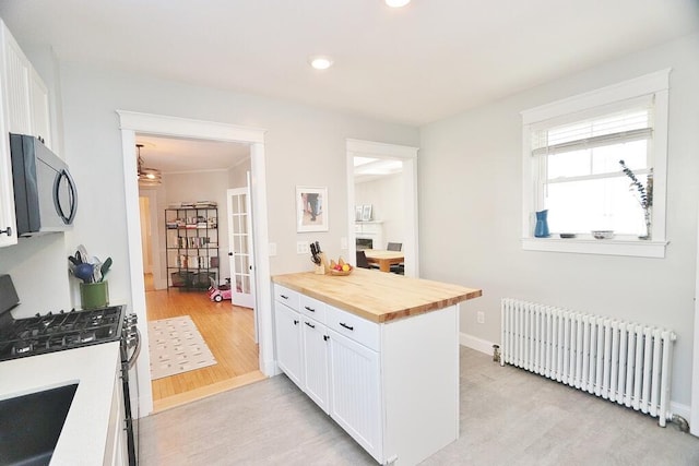 kitchen with stainless steel gas stove, white cabinets, radiator, butcher block counters, and light wood-type flooring