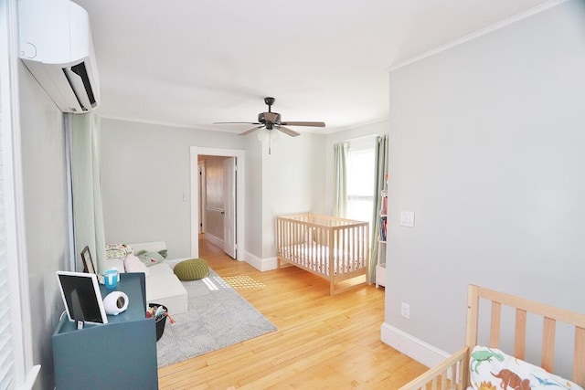 bedroom with baseboards, light wood-style flooring, ceiling fan, ornamental molding, and a wall mounted AC