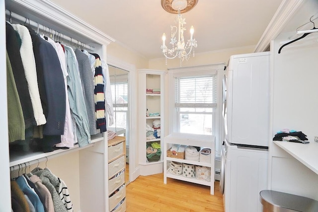 spacious closet with light wood-type flooring, stacked washer / drying machine, and an inviting chandelier