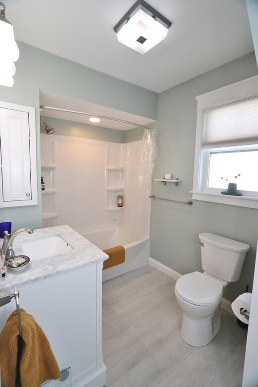 full bath with toilet, shower / bath combo, vanity, wood finished floors, and baseboards