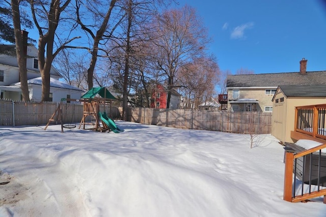 snowy yard featuring a fenced backyard and a playground