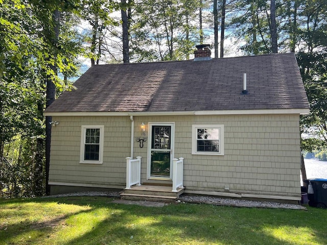 new england style home with a shingled roof, a chimney, and a front lawn