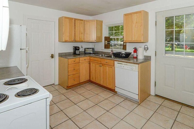 kitchen with white appliances, dark countertops, a sink, and light tile patterned flooring