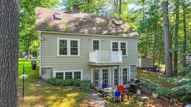 rear view of property featuring a balcony, roof with shingles, a chimney, and french doors