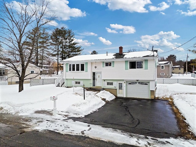 split foyer home featuring driveway, an attached garage, and fence