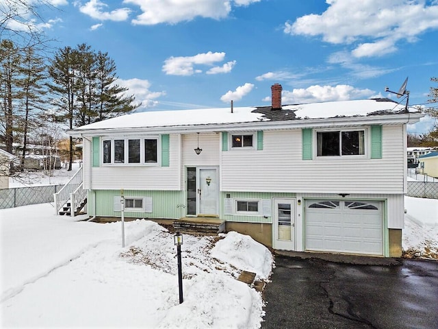 bi-level home with an attached garage, driveway, a chimney, and fence