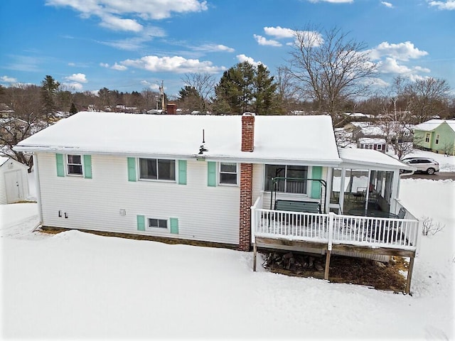 snow covered rear of property featuring a sunroom and a chimney