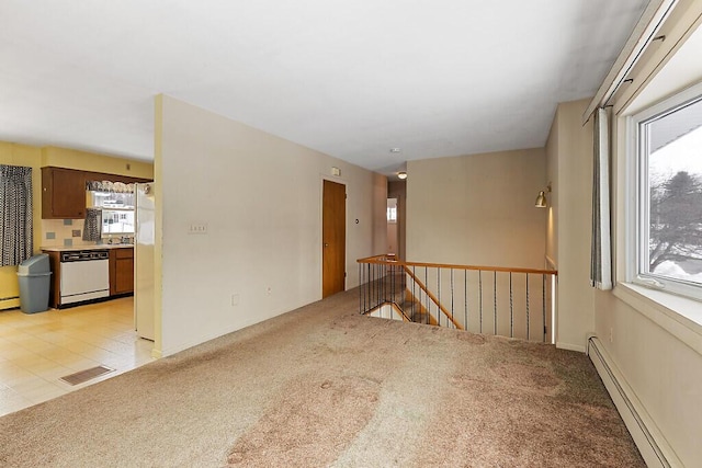 spare room with a baseboard heating unit, light carpet, and visible vents