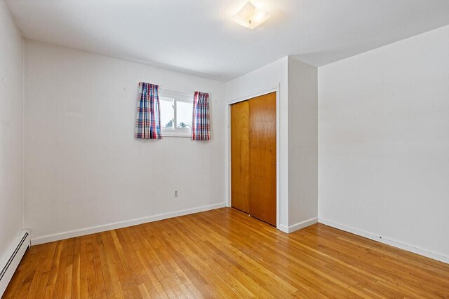 unfurnished bedroom featuring baseboards, baseboard heating, a closet, and light wood-style floors