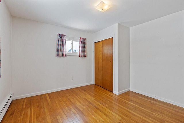 unfurnished bedroom featuring light wood-type flooring, a baseboard radiator, baseboards, and a closet