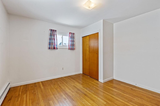 unfurnished bedroom with light wood-type flooring, a closet, a baseboard radiator, and baseboards