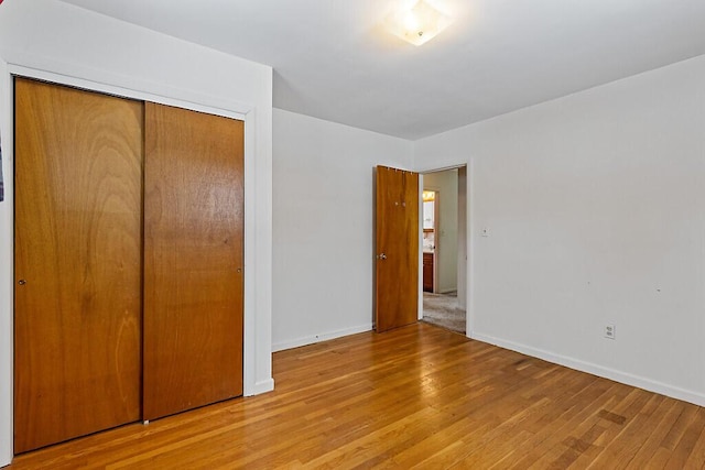 unfurnished bedroom featuring light wood finished floors, baseboards, and a closet