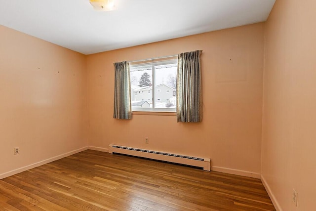 unfurnished room featuring a baseboard heating unit, baseboards, and wood finished floors