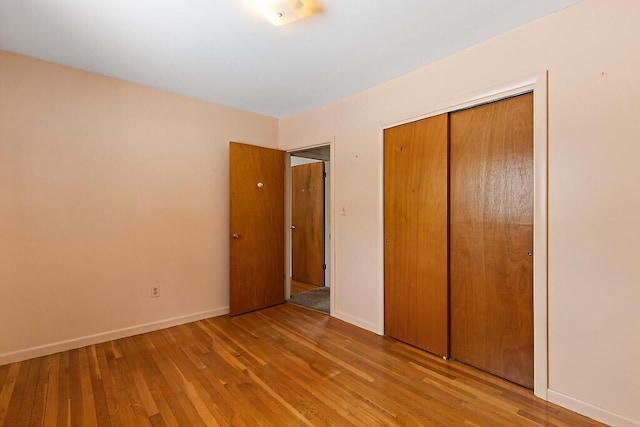 unfurnished bedroom with hardwood / wood-style floors, a closet, and baseboards