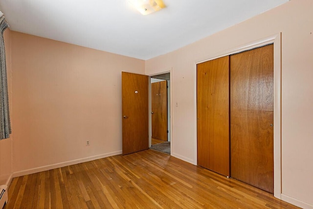 unfurnished bedroom with a closet, wood-type flooring, a baseboard radiator, and baseboards