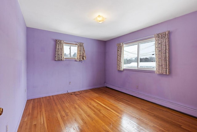 empty room featuring light wood-style floors, a baseboard radiator, and baseboards