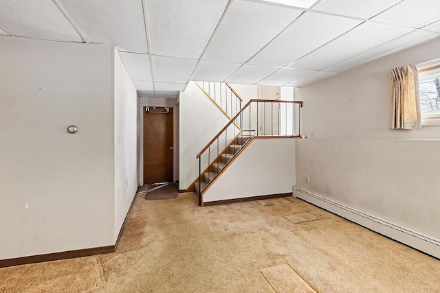 basement with a drop ceiling, a baseboard heating unit, carpet flooring, baseboards, and stairway